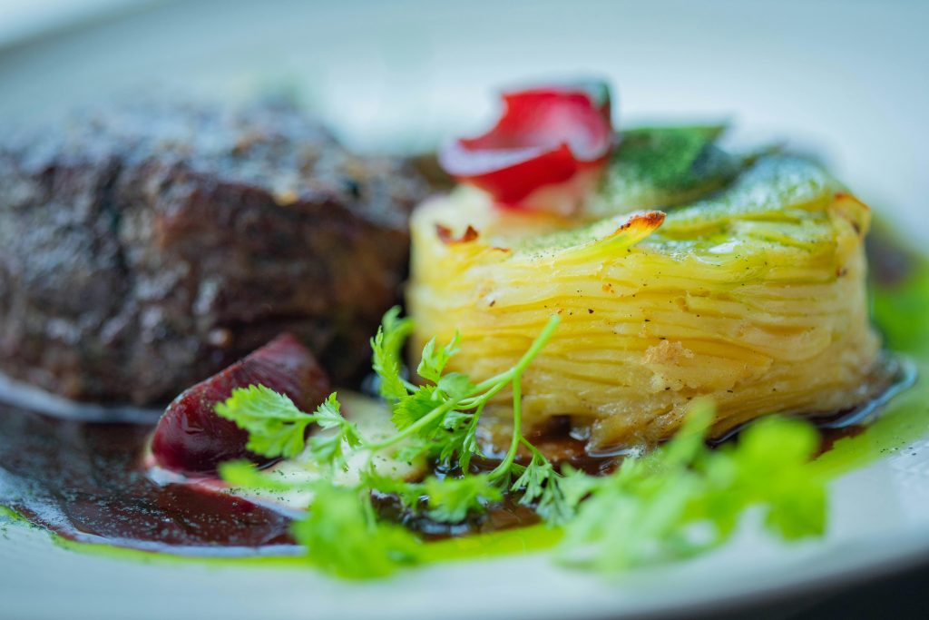 Delicious gourmet meal featuring filet mignon and herb-garnished potato gratin, perfect for fine dining.